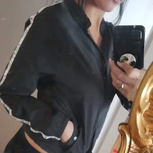 Täckjacka  - Enkelt svart täckjacka med vit rand med text på både armarna, strl xs.. Köpare står för frakt 