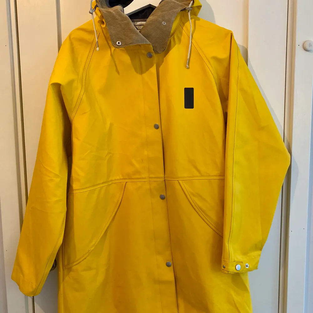 En sparsamt använd regnkappa i lite längre modell. Detaljer av manchester likande typ i kragen, snörning i huvan för att justera storleken. Den har både blixtlås och knappar. Köparen står för frakten.. Takit.
