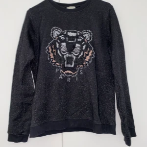Kenzo Paris sweatshirt  - Svart och lite glittrig Kenzo sweatshirt. Bilderna är tagna med blixt för att glittret ska synas. Den är från barnavdelningen men är som storlek S. Funkar på xs och M beroende på hur man bil att den ska sitta. Buda i chatten.