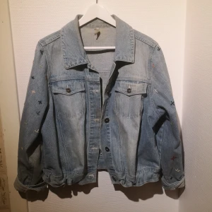 Broderad jeansjacka  - Jacka, i köpt på myrorna, som jag själv broderat blommor på. Jag har själv fixat så man kan skjustera passform längst ner på jackan. 