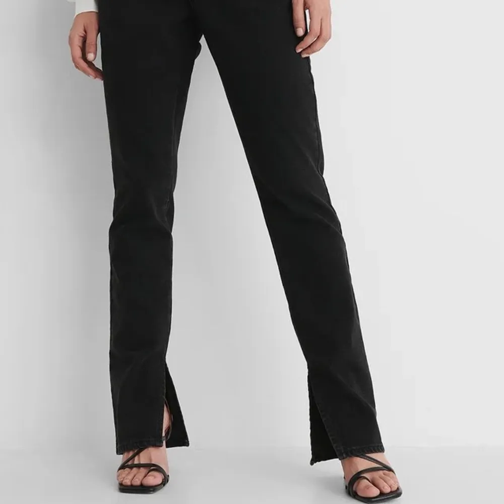 Säljer ett par helt oanvända, raka svarta denim jeans med hög midja, slits nertill och detalj upptill. Storlek 34.. Jeans & Byxor.