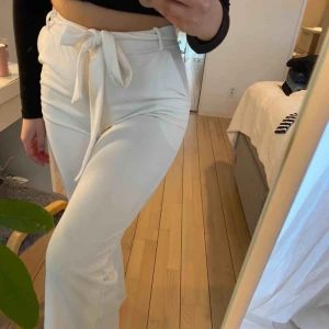 Vita kostymbyxor från Nelly - Oanvända, fodrade kostymbyxor från Nelly. Inte genomskinliga. Högmidjade med vida ben. Skärp/ band medföljer, men man kan ersätta det med eget skärp. Stretchigt material, skulle säga att de passar M-L. Köparen står för frakt💖 budet ligger på 100kr + frakt