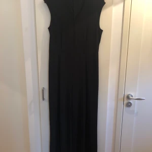 Byxdress - Svart byxdress med liten öppning över bröstet. Använd fåtal gånger. Storlek 40. Fint skick! Ordinarie pris var 399kr. Buda i kommentarerna så skriver jag privat till den med bäst pris. Leverans om i närheten men om frakt betalar köparen. 