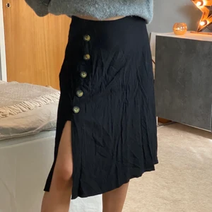 Långkjol med slits  - Svart långkjol med slits och knappar på sidan. Dragkedja i midjan. Storlek: 38. Buda i kommentarerna eller skriv till mig privat! Frakt tillkommer om mötas inte är möjligt!  
