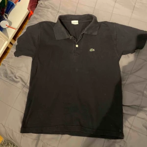  - En svart Lacoste med grön logga  Stl. M