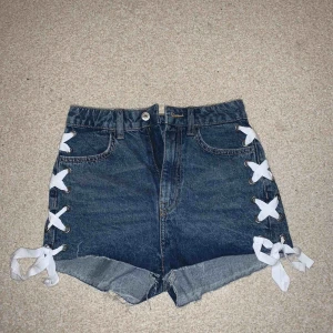  - Ett par jeans färgade shorts med vit snörning på sidorna, dem är lite fransiga nertill, fickor bak och fram aldrig använt!