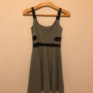  - Väldigt figurnära grå klänning från H&M med svarta detaljer på sidan. Dragkedja i rygg. Svarta axelband. Storlek XS. Går till strax över knäna. Frakt tillkommer!