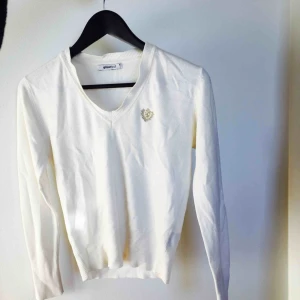 - Supersnygg långärmad vit tröja med broderat märke i guld. Bra skick! Frakt 20kr