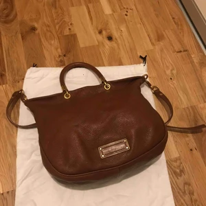  - Väska Marc Jacobs ”too hot to handle” i brunt läder med gulddetaljer. Inuti finns ett fack med dragkedja samt två mindre öppna fack. Väskan är i fint skick med någon liten skönhetsfläck. Dustbag medföljer. 