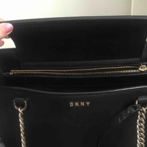  - DKNY väska i matt. Snål använd. Nypriset på denna modell ligger på 3000kr. Fodral följer med. Skickar bilder på olika delar av väskan vid intresse. Kan gå ner i pris vid snabbköp. Dubbla handtag,Innerfickor med dragkedja, Dubbla fack, Mått 36x24x11cm.