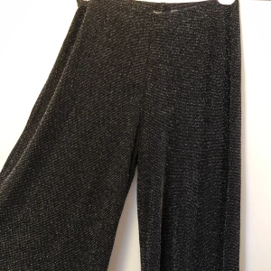 Glittriga byxor - Glittriga byxor med vida och långa ben. Aldrig använda. EJ genomskinliga. Är i ett set tillsammans med toppen i samma glittriga mönster/färg. Hela setet 100kr