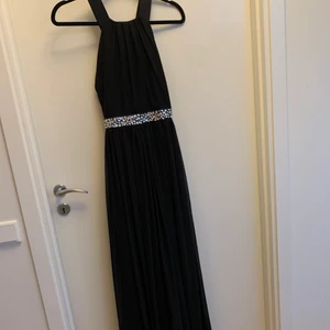 Balklänning  - Svart lång/balklänning, med ”kristallbälte” och korsad rygg. Säljer då jag inte kommer anvönda den igen, använd en gång. Nypris 899 kr men finns inte att köpa längre. Är inte helt säker på storleken, men ungefär 38/S-M. 