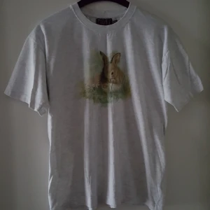  - Vintage ljusgrå, melerad t-shirt med en kanin på. Storlek 150/160 men sitter som ca S/M. Fraktkostnad blir 45kr.
