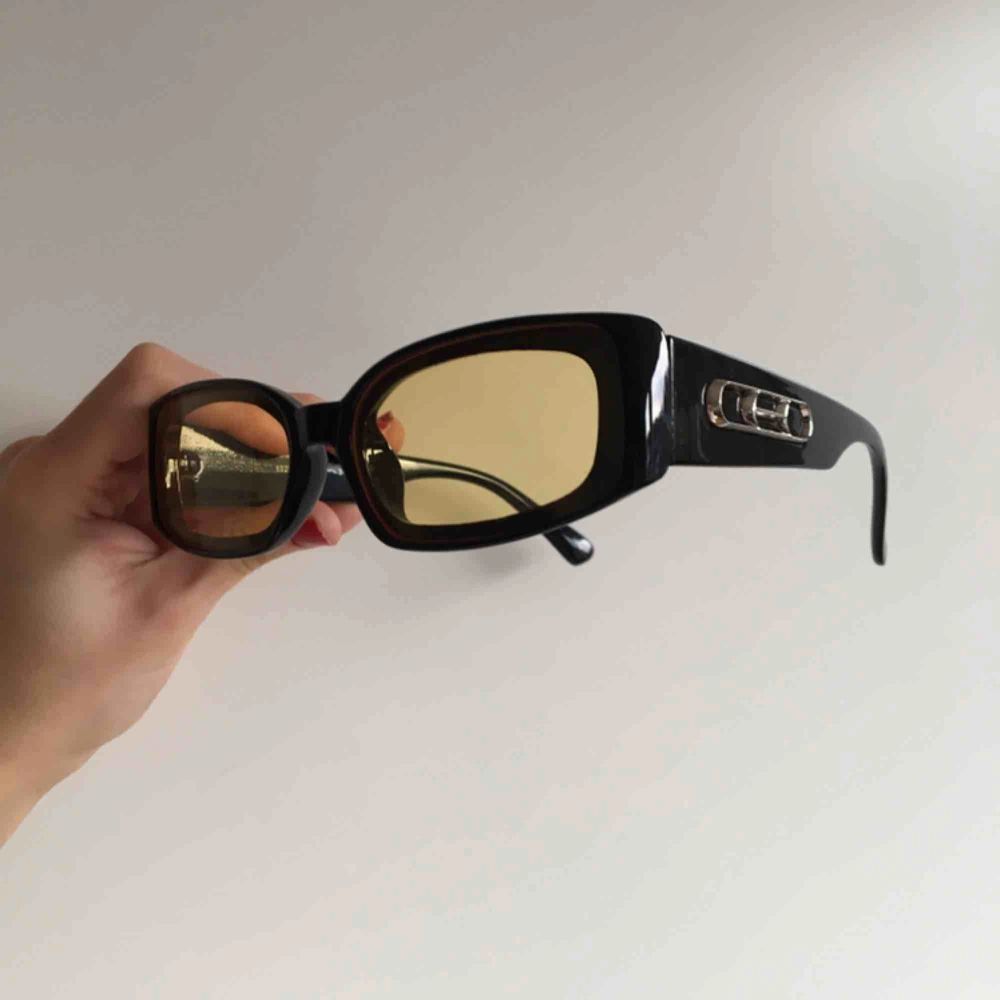 Solglasögon med gult glas och tjocka svarta bågar.. Accessoarer.