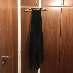 - Svart assymmetrisk klänning med knyt i sidorna och öppen under armarna. Aldrig använd. Säljs pga för stor storlek. 