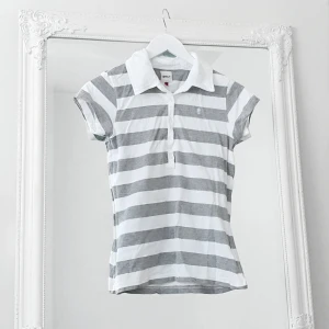 Grå vit piké t-shirt S - Färg: grå/vit.  Strl: S.   Snygg, stilren och klassisk piké t-shirt. Med logo på en bröstet. Knappar framtill. Krage. Figursydd, sitter jättesnyggt! Använd fåtal gånger.  Kommer ej till användning och stor garderobsrensning pågår! Frakt tillkommer, swish!