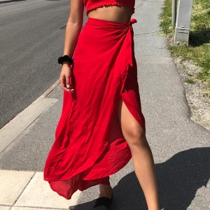 Lång kjol - Lång röd fladdrig kjol som man knyter omlott i midjan. Finns även knapp på insidan. Kampanj: KÖP 3 BETALA FÖR 2