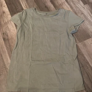 Ljusgrön t-shirt från H&M - En enkel och stilren ljusgrön t-shirt från H&M. T-shirten har rund halsringning och korta ärmar, perfekt för en avslappnad look. Tillverkad i mjukt bomullsmaterial som känns skönt mot huden.
