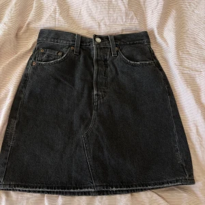 levis skirt - Säljer en svart jeanskjol från Levi's med klassisk femficksdesign och rå kant nertill. Kjolen har knapp- och dragkedjestängning framtill samt Levi's ikoniska läderpatch bak i midjan.