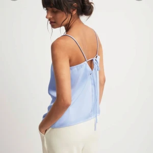 Ljusblå satin linnetopp med knytning i ryggen - Säljer en ljusblå linnetopp i satin med tunna axelband och snygg knytning i ryggen. Ny, prislapp kvar!