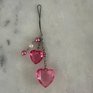  mobilhänge med Brustet hjärtan  - Säljer ett sött mobilhänge med två stora Brustet rosa hjärtan i plast och tre pärlor i rosa och vitt. Hänget har en silverfärgad kedja och svart snöre för enkel fastsättning. Perfekt som accessoar till mobilen eller väskan.