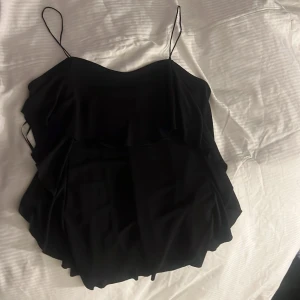 Svart volangtopp fr Gina Tricot - Säljer en svart topp från Gina Tricot med tunna axelband och volangdetaljer.