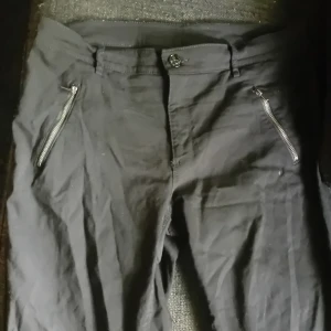 Svarta byxor med dragkedjor från KappAhl - Säljer ett par svarta byxor från KappAhl med snygga dragkedjor vid fickorna framtill. Byxorna har normal passform och raka ben. Perfekta till många olika outfits och enkla att matcha.