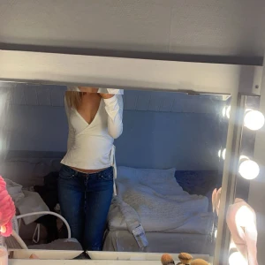 Vit omlottopp med knytband - Säljer en vit långärmad omlottopp med v-ringning och knytband i midjan från Nelly. Säljer denna då den inte kommer till användning 