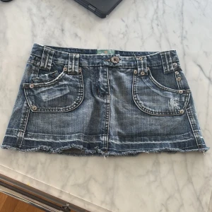 Jeanskjol mini från TRL Jeans - Säljer en kort jeanskjol från TRL Jeans i tvättad blå denim. Kjolen har rå kant nertill, stora fickor fram och bak samt slitna detaljer för en cool look. Perfekt för dig som gillar streetstyle och denim.