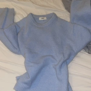 Ljusblå stickad tröja från Gina Tricot - Mysig ljusblå stickad tröja från Gina Tricot i ullblandning. Tröjan har rund halsringning och långa ärmar med ribbade muddar. Perfekt för kyliga dagar och enkel att matcha med olika outfits.