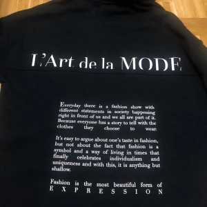 Svart hoodie med tryck från Amisu - Svart hoodie från Amisu med vit text 'L'Art de la MODE' på både fram- och baksida. Baksidan har även ett större tryck med text om mode och uttryck. Klassisk huva och lång ärm, perfekt för en stilren och trendig look. I storlek S oversized.