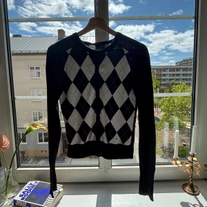 Svart och vit argyle-mönstrad kofta från J.Lindeberg - Säljer en svart och vit kofta från J.Lindeberg med klassiskt argyle-mönster. Tröjan har långa ärmar, knappar framtill och ribbade muddar. Perfekt för dig som gillar stilrena och tidlösa plagg.