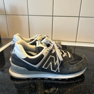 New Balance 574 sneakers - Klassiska New Balance 574 sneakers i svart med grå och vita detaljer. Skorna har snörning, rund tå och platt sula. Ovandelen är i mocka och syntet med tydlig New Balance-logga på sidan. Perfekta för en sportig och avslappnad stil. Storlek 40, 25,5cm. Inte mycket använda. Väldigt fint skick! 