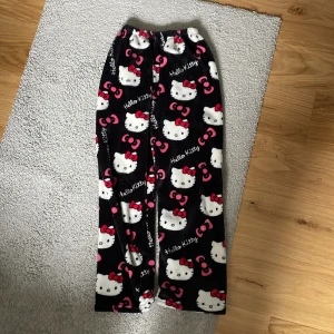 Hello Kitty mjukisbyxor i fleece - Supergosiga svarta mjukisbyxor med Hello Kitty-motiv och rosa detaljer. Byxorna har resår i midjan och är gjorda i mjuk fleece, perfekta för att chilla hemma. Sött tryck med Hello Kitty och rosetter över hela byxan.