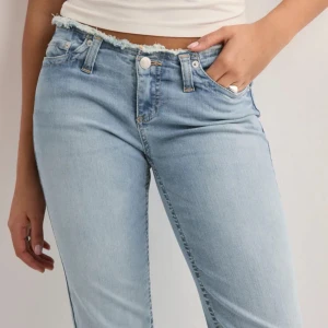 Ljusblå bootcut jeans Nelly  - Säljer ett par ljusblå jeans med bootcut passform och rå, fransig kant upptill. Jeansen har klassisk femficksdesign, knapp- och dragkedjegylf samt en snygg tvättad look. Använt 2 gånger men de blev fel storlek 