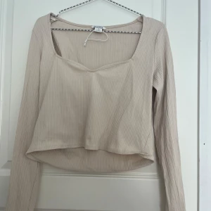 Topp - Säljer en söt beige ribbad långärmad topp från Monki med croppad passform och snygg v-ringning. Knappt använd🥰