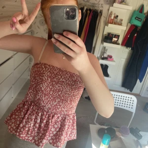 Rosa blommig croppad tubtopp - Söt rosa tubtopp med vita blommor och volang nertill. Smockad upptill för en tight passform och volangig nederdel. Perfekt för varma dagar och enkel att styla med jeans eller kjol. Tidigare snören har klippts bort. Pris går att diskutera! ☺️