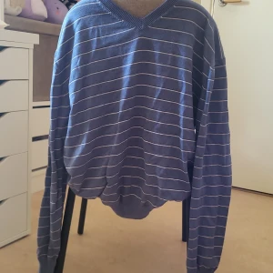 Blå randig stickad tröja - Säljer en blå stickad tröja,med tunna vita ränder och v-ringad hals. Tröjan har långa ärmar och ribbade muddar vid ärmslut och nederkant. Använd men jete bra skick inga fläckar eller hål🤍🌺