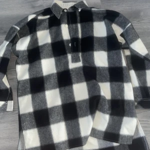 Svartvit rutig skjorta med krage - Säljer en oversized skjorta med stora svartvita rutor och klassisk krage. Skjortan har långa ärmar och knappar framtill. Perfekt för dig som gillar en avslappnad stil.