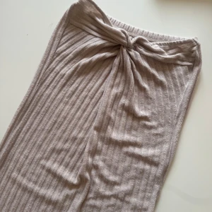 Beige ribbad kjol med knyt - Säljer en beige ribbad kjol med knyt framtill. Kjolen har en rak passform och är tillverkad i ett mjukt, stickat material som känns skönt mot huden. 