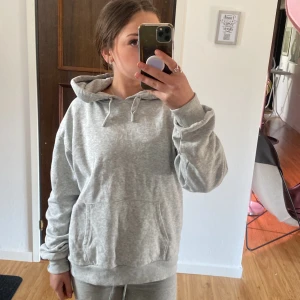 Ljusgrå hoodie - Mysig ljusgrå hoodie med huva och dragsko. Tröjan har en klassisk känguruficka framtill och ribbade muddar vid ärmslut och nederkant. Perfekt för en avslappnad stil.