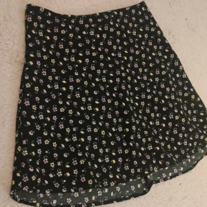 Blommig kjol  - Supersöt svart kjol från H&M Divided med små blommor i lila, vitt och gult. Kjolen har en kort passform och dragkedja i sidan. Storlek 34, alltså XS💗