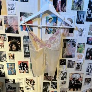 Vit och rosa spetslinnetopp - Söt vit linnetopp med tunna axelband och spetsdetaljer i rosa och vitt längs urringningen. Toppen har en liten rosett framtill och är croppad i modellen. Perfekt för lager-på-lager eller sommaroutfits.