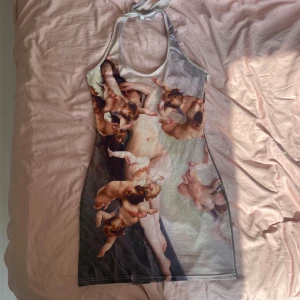 Klänning med änglamotiv - Unik klänning med konstnärligt tryck av änglar och klassiskt motiv. Figurnära passform och ärmlös design med halterneck. Perfekt för dig som vill sticka ut med ett kreativt men elegant plagg. Stretchigt tyg så passar de flesta, själv är jag XL och kan ha den utan problem.