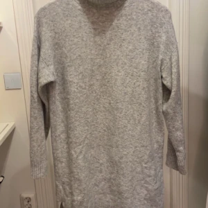 Ljusgrå stickad polotröja - Mysig ljusgrå stickad polotröja med lång ärm. Perfekt för kyliga dagar. Man kan även ha den som en klänning då den är lång. Det är storlek 13-14 år men passar xs-s också