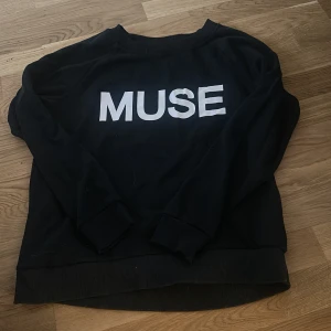 Svart sweatshirt med MUSE-tryck - Svart sweatshirt med stort vitt MUSE-tryck på bröstet. Tröjan har långa ärmar, rund halsringning och ribbade muddar vid ärmslut och nederkant. Perfekt för dig som gillar enkel och stilren design.