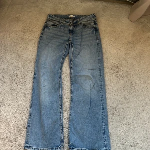 Blå wide jeans från Gina Tricot - Säljer ett par ljusblå jeans från Gina Tricot med breda ben och låg midja. Jeansen har klassiska fem fickor, dubbla knappar i midjan och snygga detaljer på bakfickorna. Perfekta för en avslappnad och trendig look.