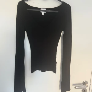 Svart ribbad långärmad tröja H&M - Svart långärmad tröja från H&M med v-ringad hals och ribbad struktur. Tröjan är tight i modellen och har en smickrande passform som framhäver figuren. Perfekt att styla med jeans eller kjol för en clean look.
