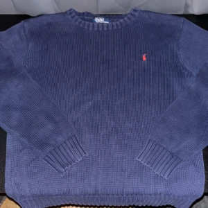 Blå stickad tröja från Polo Ralph Lauren - Säljer en klassisk blå stickad tröja från Polo Ralph Lauren. Tröjan har rund halsringning, långa ärmar och den ikoniska röda broderade loggan på bröstet. Inget fel på den förutom att den är lite urtvättad som syns på bilderna, inget som syns på avstånd eller något man tänker på!                         Hör av er vid minsta fundering 🤗