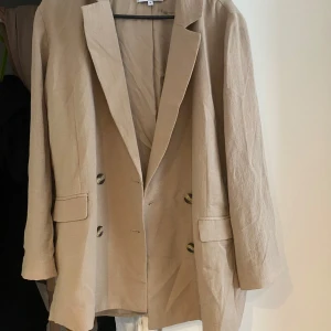 Beige kavaj från Weekday, stl 38 - Stilren beige kavaj från Weekday i storlek 38. Dubbelknäppt med snygga knappar och två fickor med lock framtill. Rak passform och lätt material som ger en avslappnad men ändå dressad look.